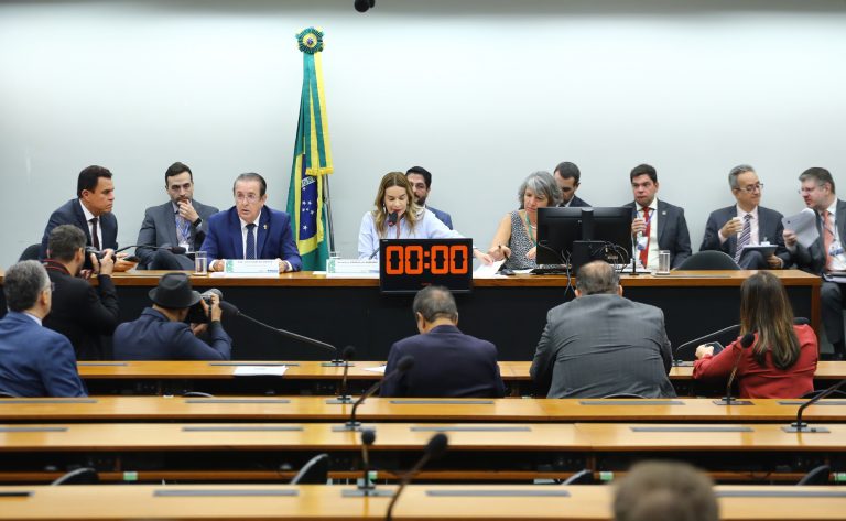 Senadora Daniella Ribeiro fala ao microfone. Ela é uma mulher clara com cabelo loiro e comprido e veste uma blusa marfim