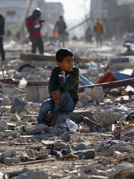 Criança palestina sentada entre os escombros de casas destruídas num ataque israelense em Khan Younis, no sul da Faixa de Gaza.