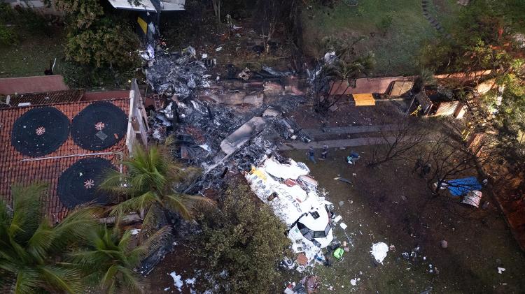 Imagem aérea mostra um gramado com destroços de um avião branco e do lado direito o telhado de uma casa